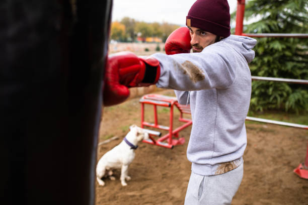 un jeune boxeur jetant un coup de poing féroce à un sac de poinçonnage - men sweat combative sport boxing photos et images de collection