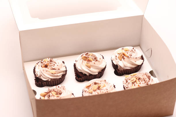 istock Six chocolate muffins with white cream and peanuts in an open box. Sweets on a white table 1285320171