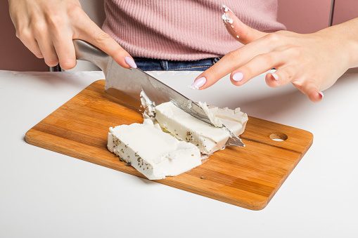 a woman cuts feta cheese into cubes on a cutting Board.