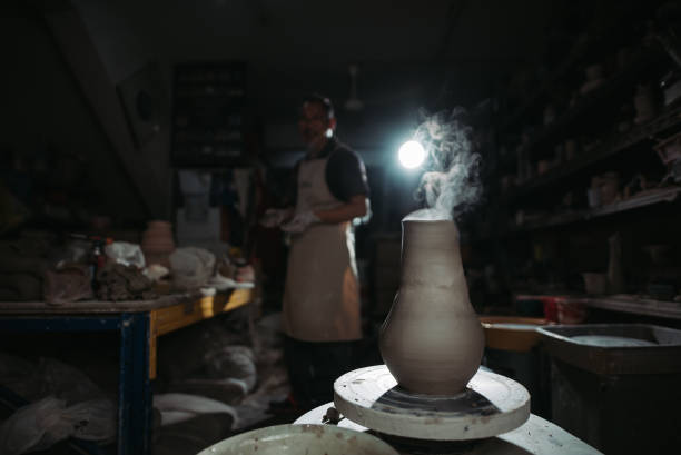 selective focus of smoke emitting from pottery on pottery wheel, owner of the pottery studio standing behind