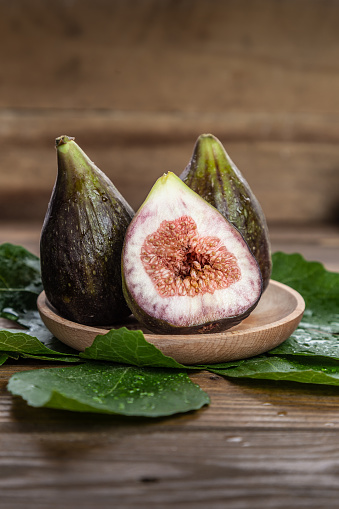 Fresh figs on wooden plate, with fig leaves, on wooden background