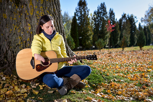 Outdoor shot of a female guitarist with disability playing a guitar. Woman has one arm, but still plays a guitar. Awareness for people with disabilities