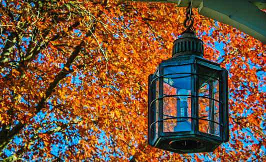 A lantern hangs from a porch on Cape Cod against a backdrop of vivid red autumn leaves.