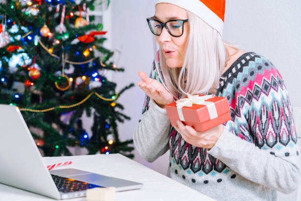 istock Christmas online family congratulations. Smiling girl at home using laptop computer notebook for video call friends and parents in Santa hat. Woman looking camera and waving greeting hands. 1285330884