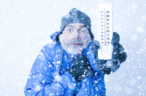 Portrait of man freezing under snowfall
He shows a thermometer to show how it's cold.