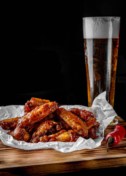 vaso de cerveza fresca y alitas de pollo fritas sobre mesa de madera sobre fondo negro - beer wing spicy chicken wings chicken wing fotografías e imágenes de stock