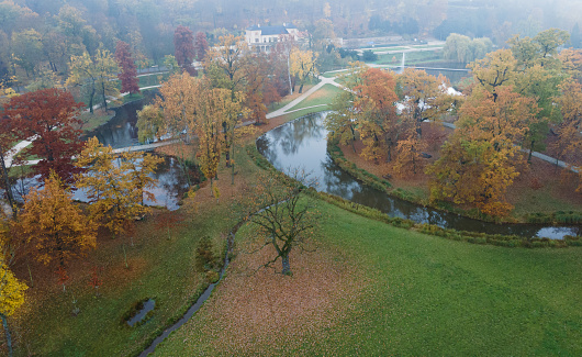 Aerial view of Stromovka public park in Prague, Czech Republic. Colorful autumnal leaves on trees, footpath and a pond. Foggy and calm early morning scenery