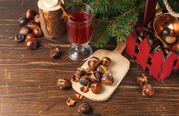 Roasted chestnuts, hot drink in a glass and fir branches on a rough wooden surface, horizontally with space stock photo