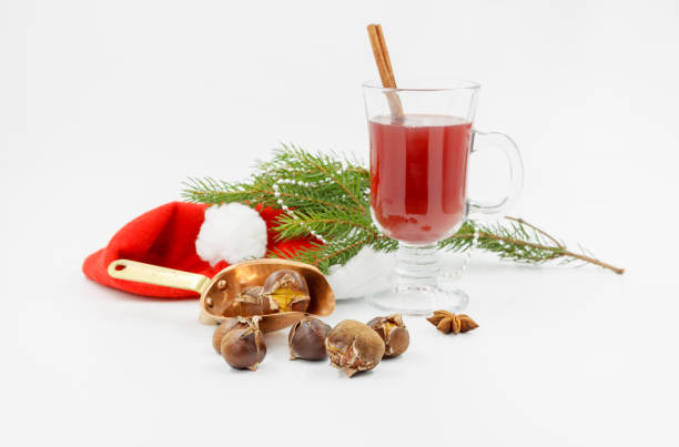 Roasted chestnuts in a copper scoop, a glass of mulled wine, a red hat and a spruce branch on a white background, horizontally with space stock photo