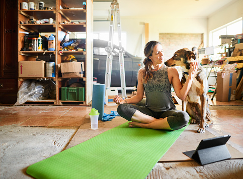 Smiling woman loving her dog after an online yoga class on a digital tablet in her garage at home