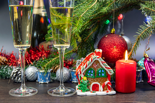 Christmas decoration with a red burning candle. Happy New Year. Two glasses of champagne with gas bubbles. Christmas gingerbread in the form of a colorful house ..