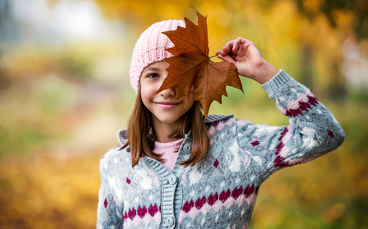 Autumn coming. Cute little girl holding yellow leaf in a hand