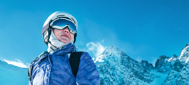 Skier female portrait in safe ski helmet and goggles with picturesque snowy Tatry mountains background.