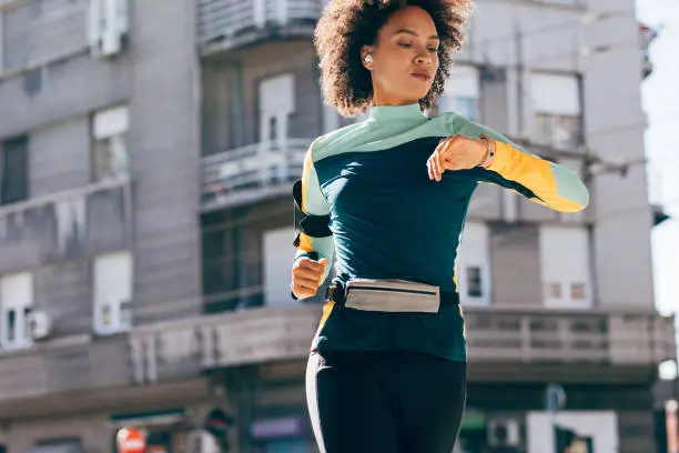Morning routine: a health conscious woman running in the streets and checking her pace on her smart watch
