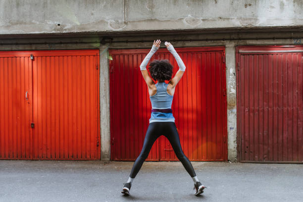 Anonymous Female Athlete with an Afro Haircut Doing Jumping Jacks Outdoors Morning routine: fit Afro American woman exercising outdoors Jumping Jacks stock pictures, royalty-free photos & images