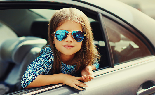 Portrait close up of little girl child sitting in a car as passenger looking out of car window