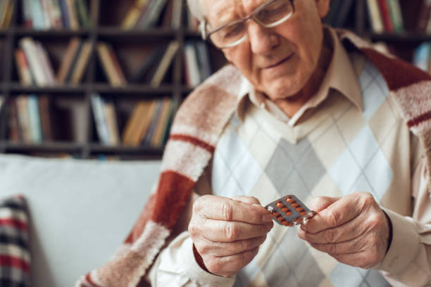 istock Senior man alone sitting at library sick covered with plaid reading drugs name 1285369557