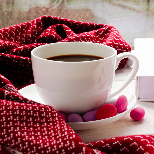 istock A white cup of coffee with multi-colored sweets stands on a wooden window sill next to a warm scarf and white book 1285374521
