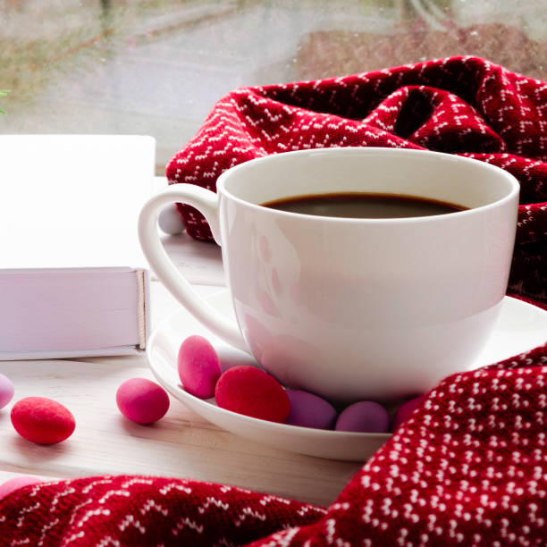 istock A cozy concept with a white cup of coffee, a red warm scarf, a book and multi-colored candy on the windowsill 1285374524