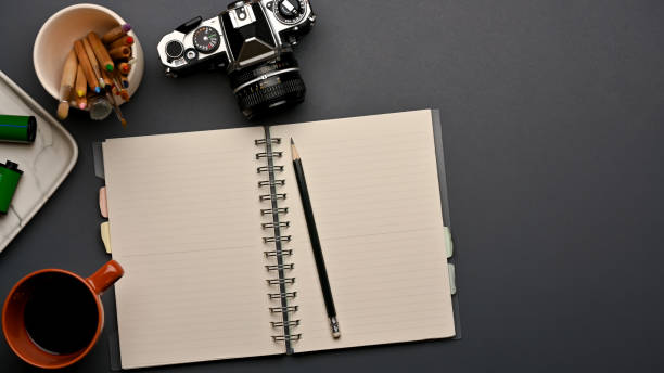 Top view of workspace with opened blank notebook, camera and supplies in home office room