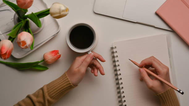 istock Female hand writing on blank notebook and holding coffee mug on home office desk 1285387684