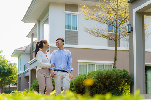 Portrait of Asian couple walking and hugging together looking happy in front of their new house to start new life. Family, age, home, real estate and people concept.