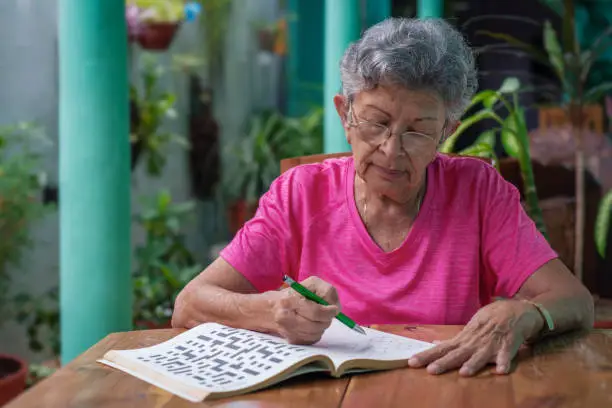 Senior woman with glasses sitting at a table, filling in a sudoku puzzle