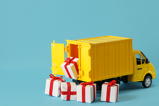 Yellow truck delivery gift box on blue background. Cargo transportation, delivery service. Transport company. Infrastructure and logistics. Unloading cardboard box.