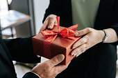 Close-up view of hands of unrecognizable woman giving red gift box tied to bow handed to man.