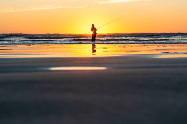 istock Fishing in the Sunset by the Pacific Ocean Shore 1285407898