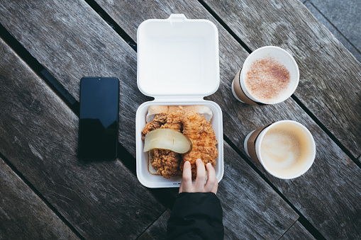 Overhead high angle view on a fried chicken with hot chocolate and coffee with a child trying to reach and grab a piece of chicken tender.