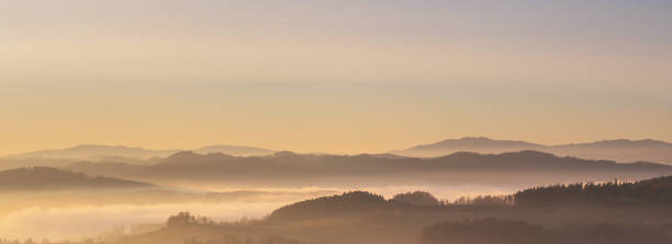 Photo of misty landscape at sunset, mountains rising from clouds of fog, clear sky
