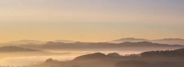 Photo of misty landscape at sunset, mountains rising from clouds of fog, clear sky