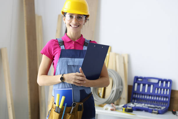istock Young woman builder in protective overalls and hard hat smiling in workshop 1285416285