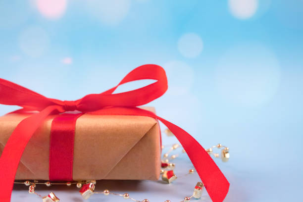 istock Front view of gift box with red bow on festive blue background with golden sparkles around and copyspace for your text. Christmas, New Year, Valentines Day or birthday celebration concept 1285416320