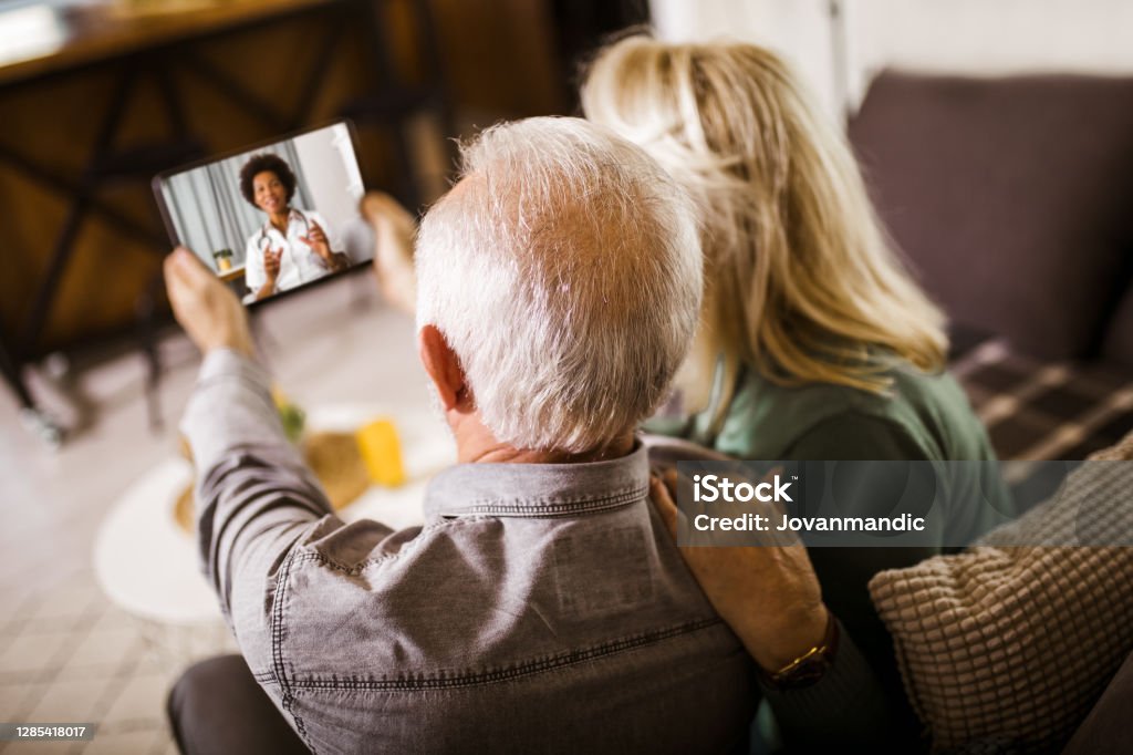 Senior couple at home holding digital tablet during video call with family doctor Telemedicine Stock Photo