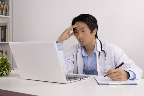 istock Serious Asian Doctor and Stethoscope Write Report and Using Laptop Computer 1285425794