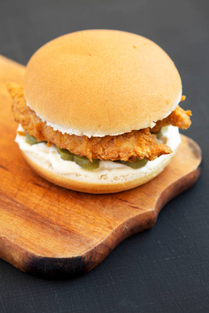 istock Homemade Burgers with fried chicken strips on a rustic wooden board on a black surface, low angle view. 1285427393