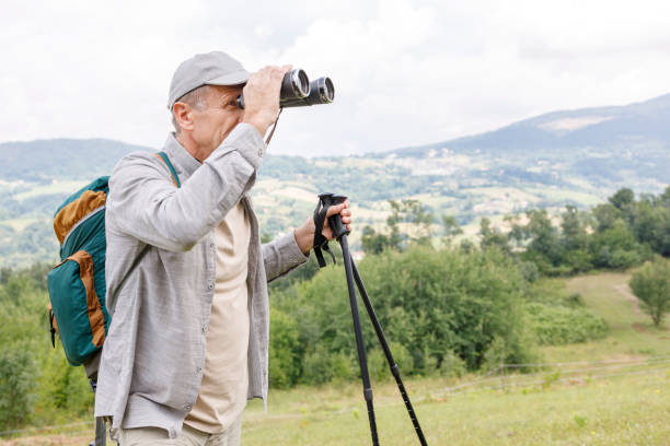 istock Old hiker holding trekking poles and looking through binoculars 1285429334