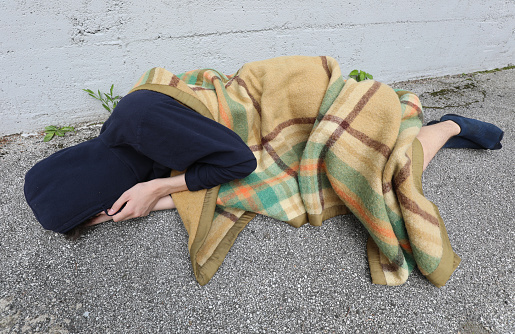 homeless as he sleeps on the floor under a filthy blanket