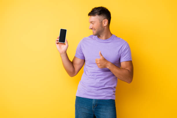 istock happy man holding smartphone with blank screen and showing thumb up on yellow 1285435507