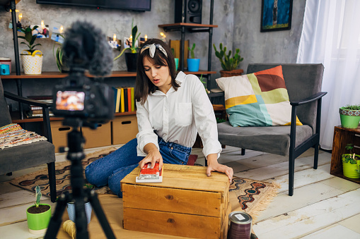 Female carpenter recording her tutorial about wood sanding and easy DIY how to paint a furniture from your home, while using camera for vlogging in her cozy home during COVID-19 pandemic