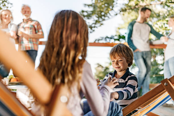 Friendly siblings sit on stone bench resting in tree shadow on summer holidays. Three blond brothers in shorts enjoy spending time together on sunny day