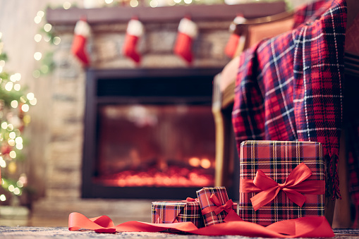 Butaca con cajas de regalo a cuadros y embalaje para familia cerca de árbol de navidad y chimenea. Vista inferior photo