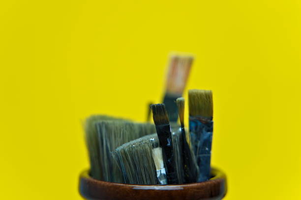 istock Used paint brushes sitting in a jar and isolated on yellow background 1285446454
