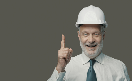 Cheerful businessman and engineer wearing a safety helmet and pointing upwards