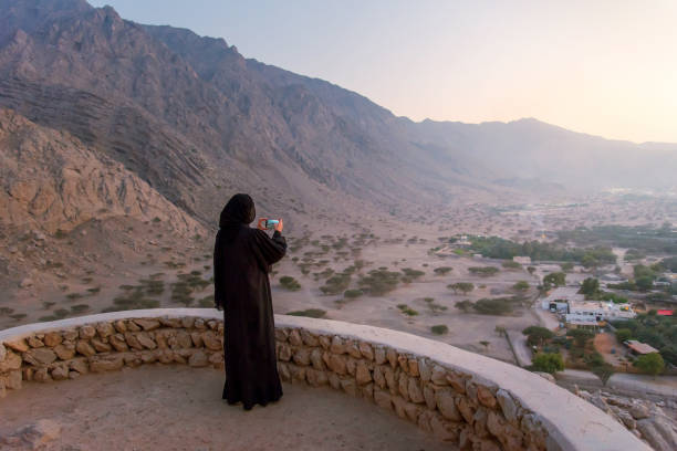 Woman in abaya visiting middle eastern fortress in the desert at sunset Woman in hijab taking photo from a middle eastern fortress in the desert of United Arab Emirates at sunset jebel hafeet stock pictures, royalty-free photos & images