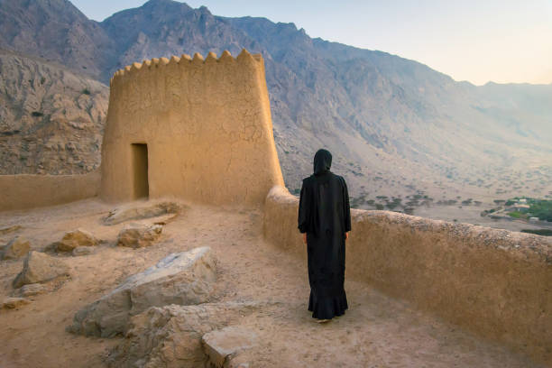 Woman in abaya visiting middle eastern Dhayah Fort in north Ras Al Khaimah, UAE in the desert at sunset Woman in hijab visiting middle eastern Dhayah Fort in north Ras Al Khaimah, United Arab Emirates in the desert at sunset jebel hafeet stock pictures, royalty-free photos & images