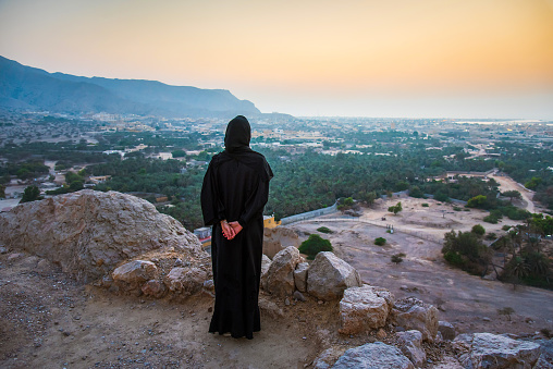 Woman in hijab looking at the sunset from a middle eastern fortress in the desert of United Arab Emirates at sunset