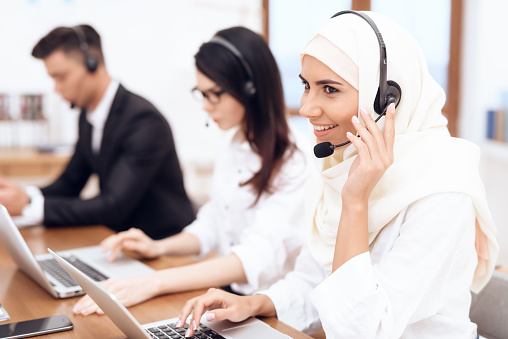 An Arab woman works in a call center. She's an operator. Her colleagues work nearby.